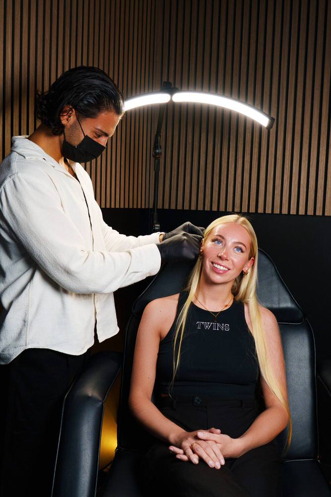 Ohr mit goldenen Piercings, umrahmt von Händen – TWINS-ATELIER Hamburg